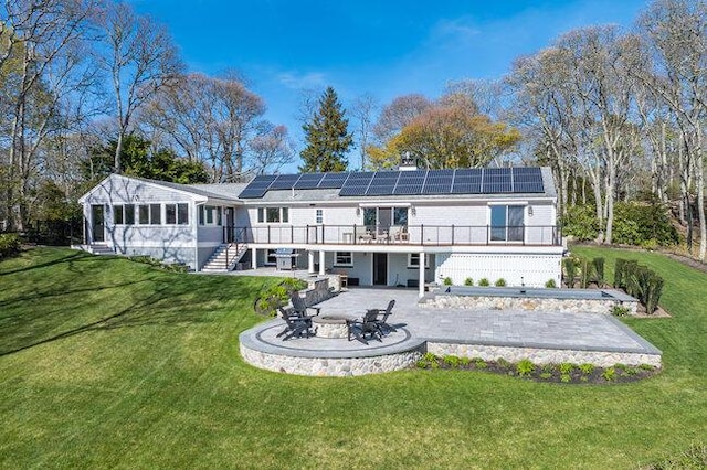 rear view of property with roof mounted solar panels, an outdoor fire pit, a wooden deck, a patio area, and stairs