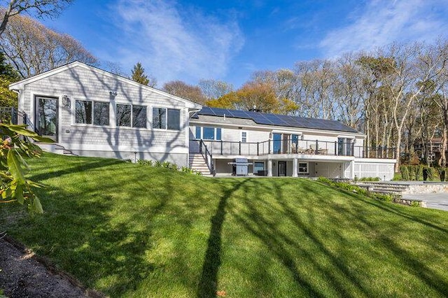 rear view of property with a yard, a deck, stairway, and roof mounted solar panels