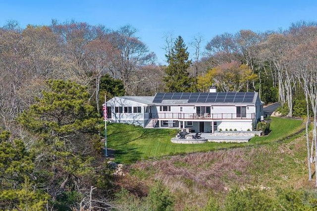 rear view of property featuring a yard, a view of trees, solar panels, a patio area, and a deck