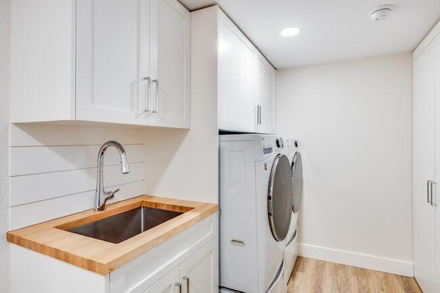 washroom featuring a sink, cabinet space, washing machine and clothes dryer, light wood-style flooring, and baseboards
