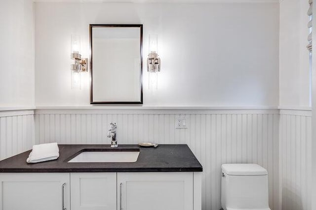 bathroom featuring wainscoting, vanity, toilet, and a decorative wall