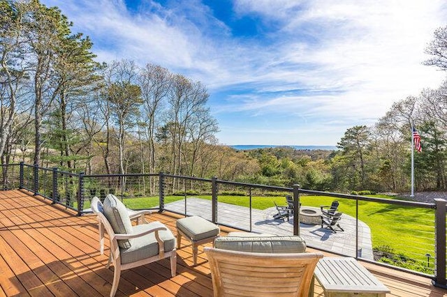 wooden terrace featuring an outdoor fire pit, a forest view, and a lawn