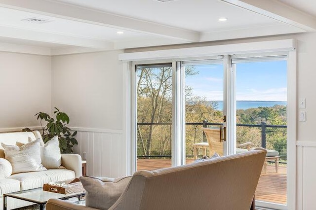living area featuring visible vents, a water view, a decorative wall, a wainscoted wall, and beamed ceiling