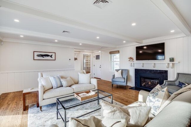 living room featuring beam ceiling, a fireplace with flush hearth, visible vents, and wood finished floors