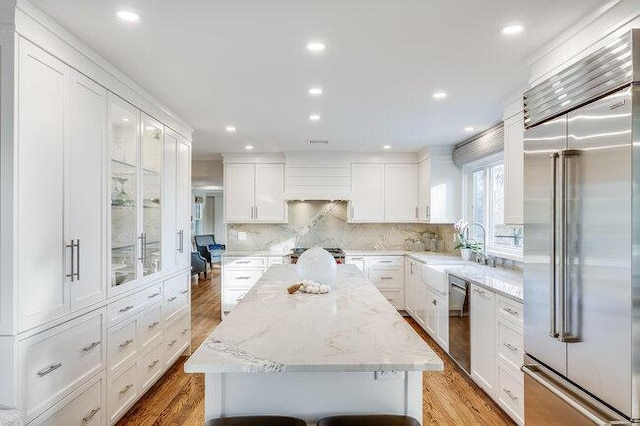 kitchen featuring appliances with stainless steel finishes, a center island, white cabinetry, backsplash, and light wood-type flooring