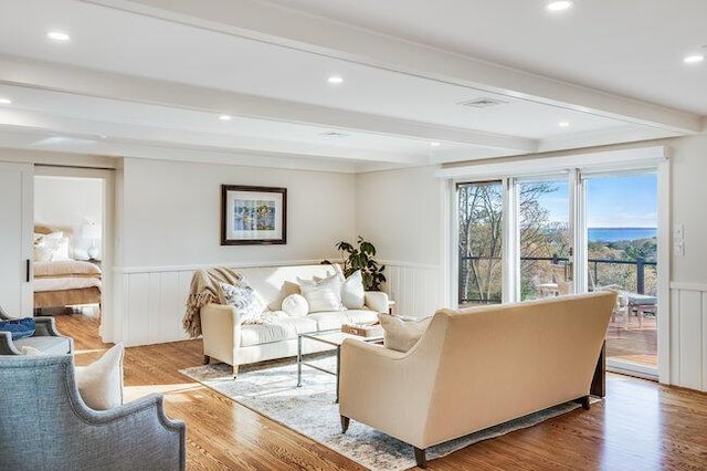 living area with a decorative wall, wood finished floors, recessed lighting, beamed ceiling, and wainscoting