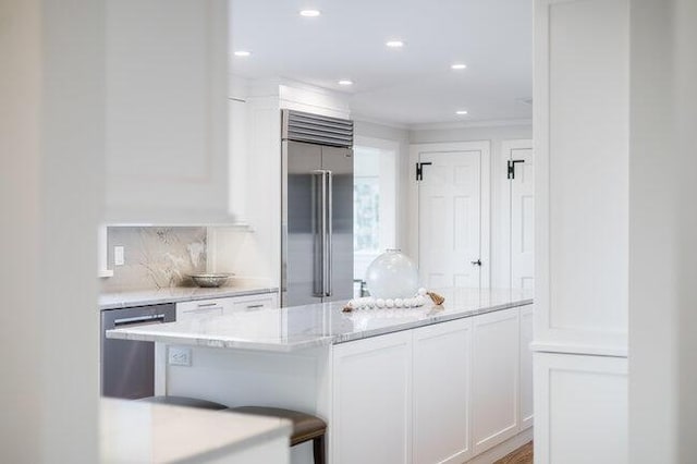 kitchen with recessed lighting, light stone counters, backsplash, white cabinets, and appliances with stainless steel finishes