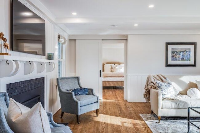 sitting room with recessed lighting, wainscoting, crown molding, wood finished floors, and a fireplace