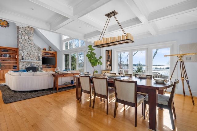 dining area featuring a stone fireplace, beamed ceiling, coffered ceiling, and light wood-style floors