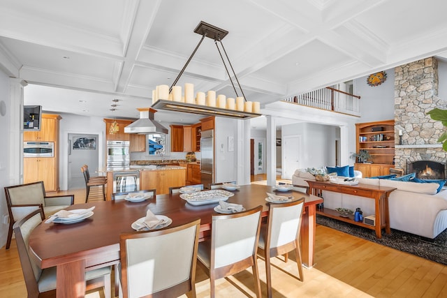 dining room with coffered ceiling, beamed ceiling, ornate columns, light wood-style floors, and a fireplace