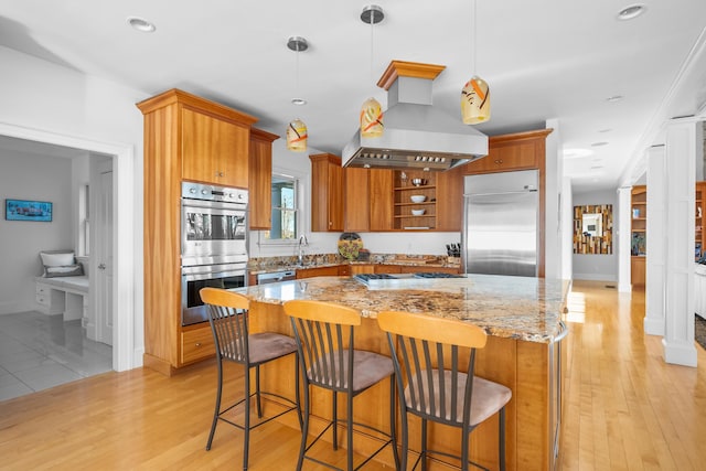 kitchen featuring light stone counters, a center island, stainless steel appliances, hanging light fixtures, and island range hood