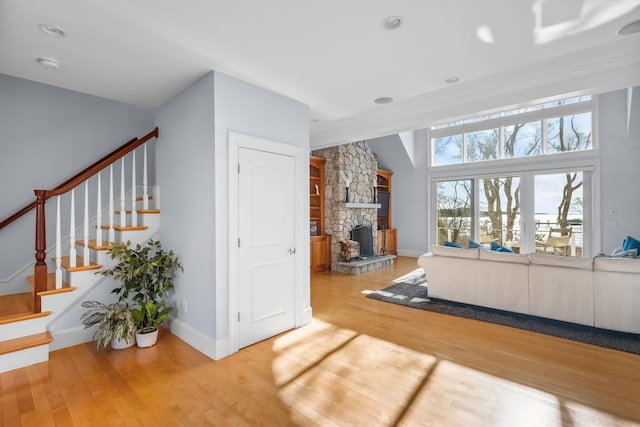 living area with light wood-style floors, stairway, a stone fireplace, and baseboards