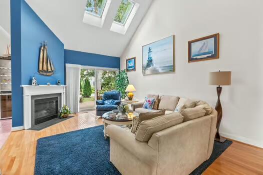 3 Mayfair Ct, Mashpee, MA 02649 - living room featuring high vaulted ceiling, a skylight, wood finished floors, and a fireplace with flush hearth