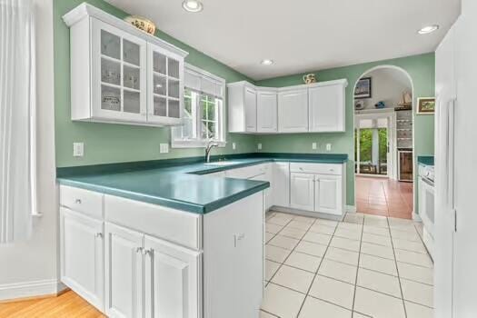 3 Mayfair Ct, Mashpee, MA 02649 - kitchen with white cabinetry, glass insert cabinets, a peninsula, dark countertops, and arched walkways