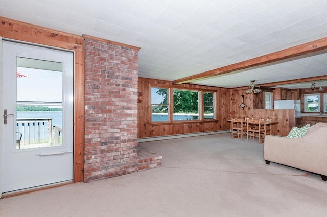 unfurnished living room featuring a water view, a wealth of natural light, a baseboard radiator, and wooden walls