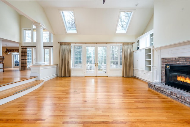 unfurnished living room featuring light wood finished floors, built in shelves, a skylight, and ornate columns