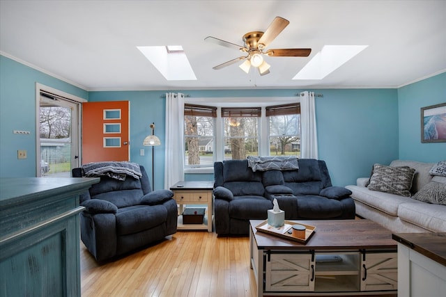living room with light wood-style floors, ornamental molding, a ceiling fan, and a skylight