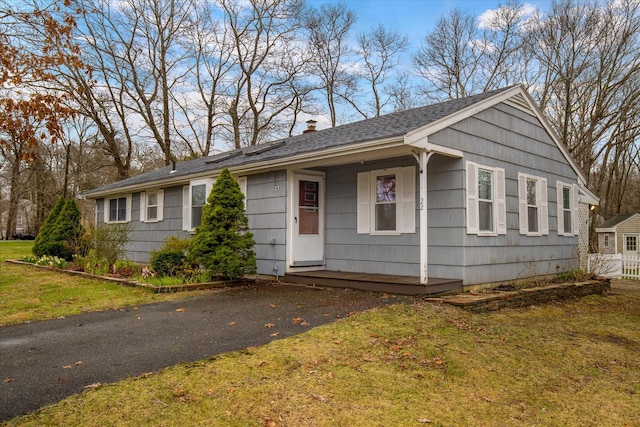 single story home with a front yard, a shingled roof, and a chimney