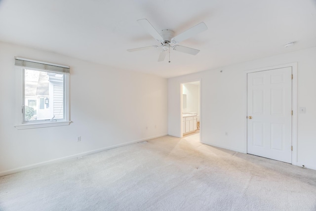 unfurnished bedroom featuring ensuite bath, light colored carpet, baseboards, and ceiling fan