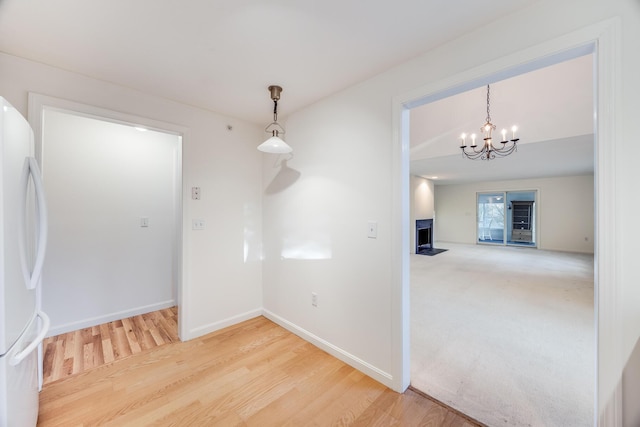 unfurnished dining area with a fireplace with flush hearth, an inviting chandelier, baseboards, and wood finished floors