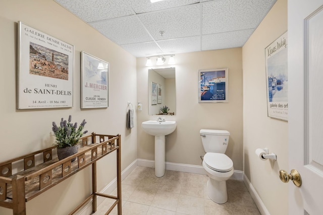 bathroom with a sink, tile patterned floors, a drop ceiling, baseboards, and toilet