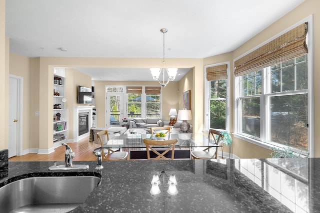 kitchen with a sink, decorative light fixtures, dark stone counters, a glass covered fireplace, and built in features