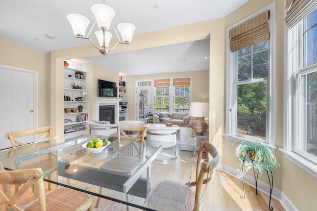 dining area featuring a glass covered fireplace, baseboards, a chandelier, and light wood-style floors