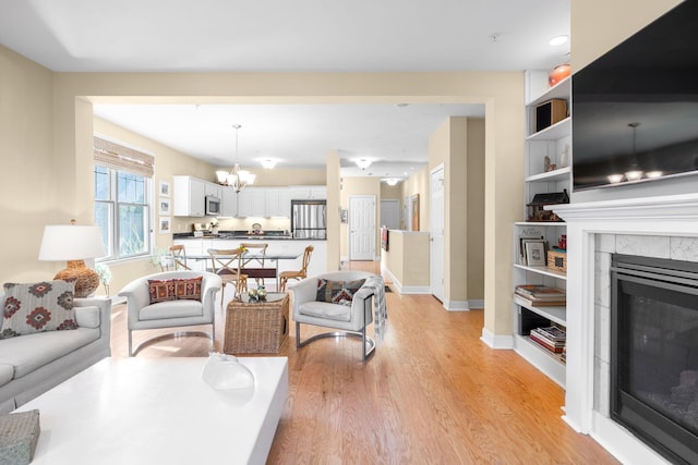 living area with light wood-style floors, built in features, a tile fireplace, baseboards, and a notable chandelier