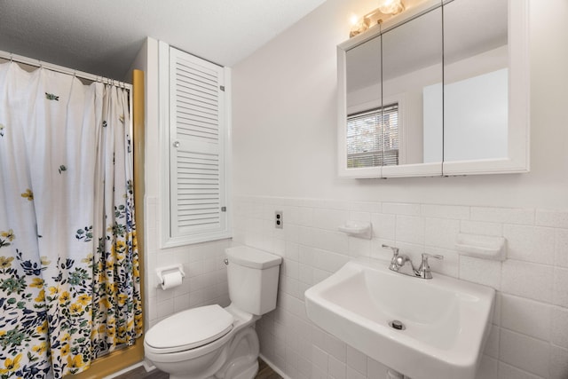 full bath with curtained shower, toilet, a sink, tile walls, and wainscoting