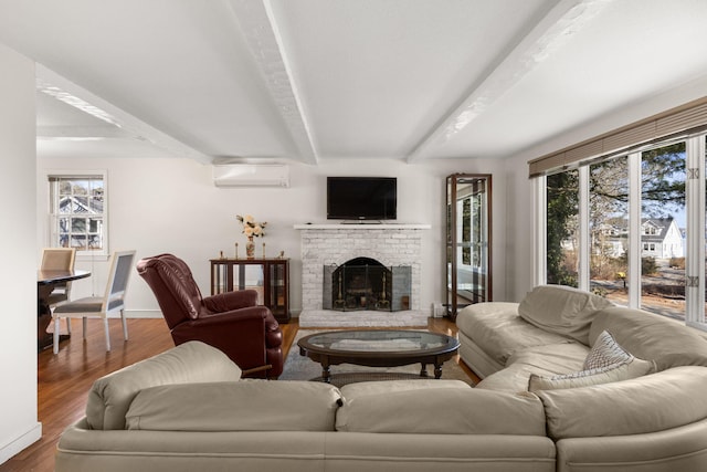 living area with beam ceiling, a wall mounted AC, a brick fireplace, wood finished floors, and baseboards