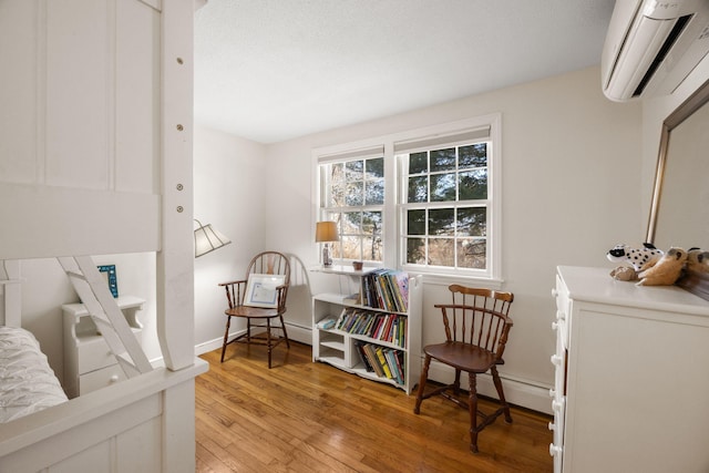 living area featuring light wood finished floors, a wall mounted air conditioner, a baseboard radiator, and baseboards