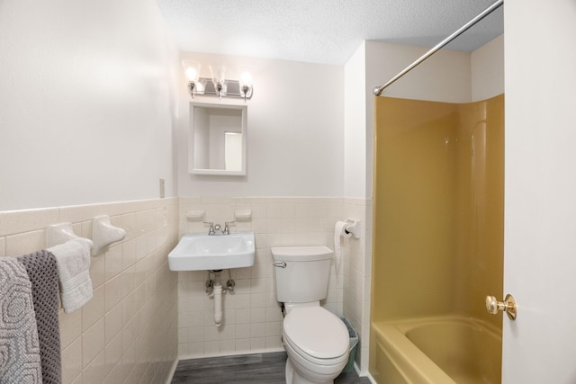 full bath with a textured ceiling, a wainscoted wall, toilet, and tile walls