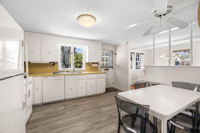 kitchen with light wood-style flooring, white appliances, white cabinetry, light countertops, and hanging light fixtures