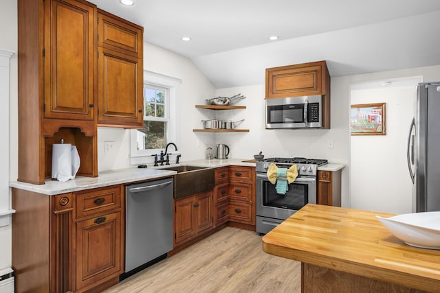 kitchen with light wood-style flooring, appliances with stainless steel finishes, brown cabinetry, vaulted ceiling, and a sink