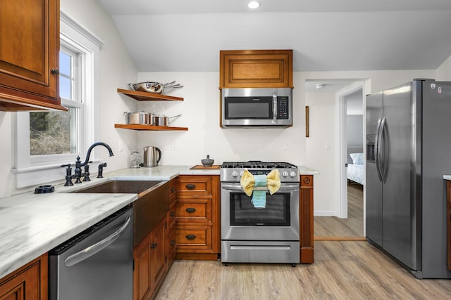 kitchen with a sink, light countertops, appliances with stainless steel finishes, brown cabinets, and light wood finished floors