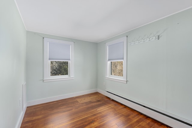 empty room with a baseboard heating unit, dark wood-style flooring, baseboards, and a healthy amount of sunlight