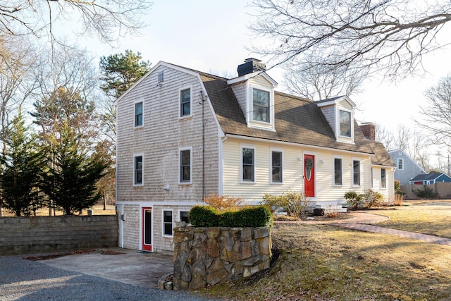 view of front of home with roof with shingles, a chimney, fence, and a gambrel roof