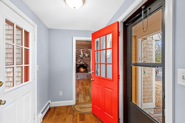 doorway with a brick fireplace, a baseboard radiator, baseboards, and wood finished floors