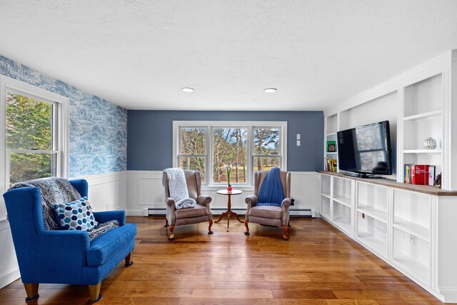 sitting room with a wainscoted wall, plenty of natural light, wood finished floors, and wallpapered walls