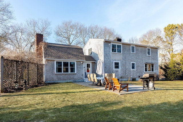 rear view of property with a shingled roof, a patio area, a lawn, and a chimney