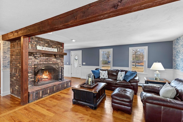 living area featuring wainscoting, hardwood / wood-style flooring, beamed ceiling, baseboard heating, and a fireplace