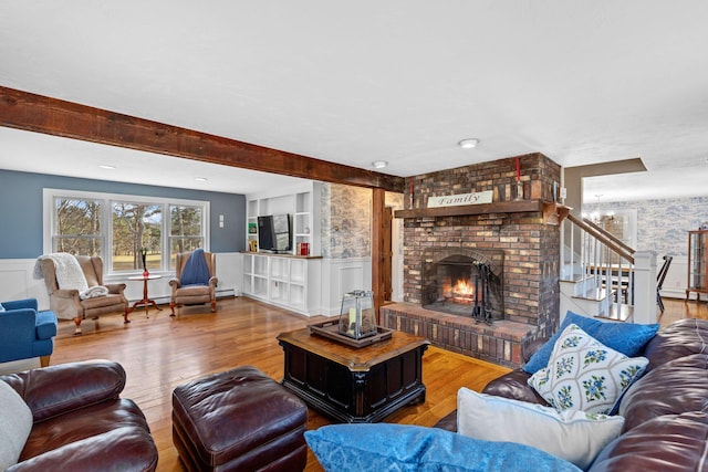 living area featuring a decorative wall, stairway, a brick fireplace, wainscoting, and wood finished floors