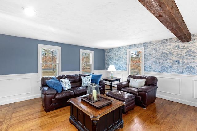 living area featuring light wood-style floors, a wainscoted wall, beamed ceiling, and wallpapered walls