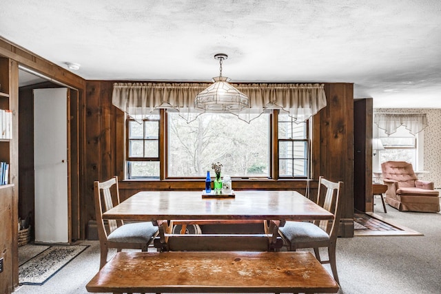 carpeted dining area featuring wood walls and a textured ceiling