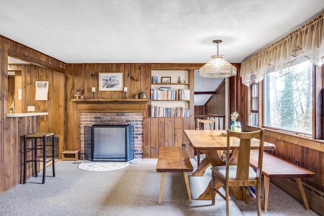 dining room featuring a textured ceiling, wood walls, carpet floors, and a brick fireplace