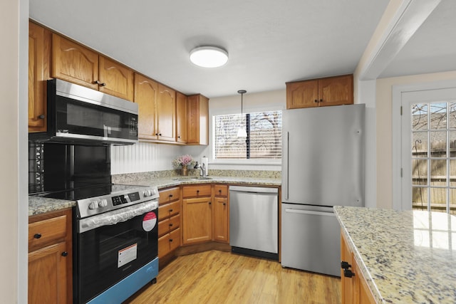 kitchen with brown cabinets, light stone counters, a sink, stainless steel appliances, and light wood-type flooring