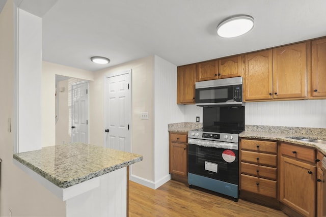 kitchen featuring light stone countertops, brown cabinets, light wood-type flooring, baseboards, and stainless steel appliances