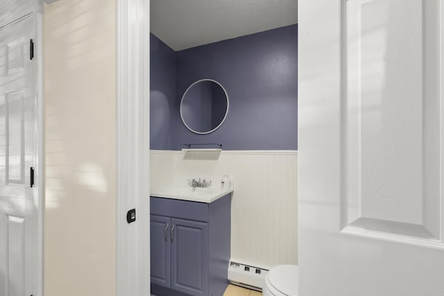 bathroom with vanity, toilet, baseboard heating, and a wainscoted wall