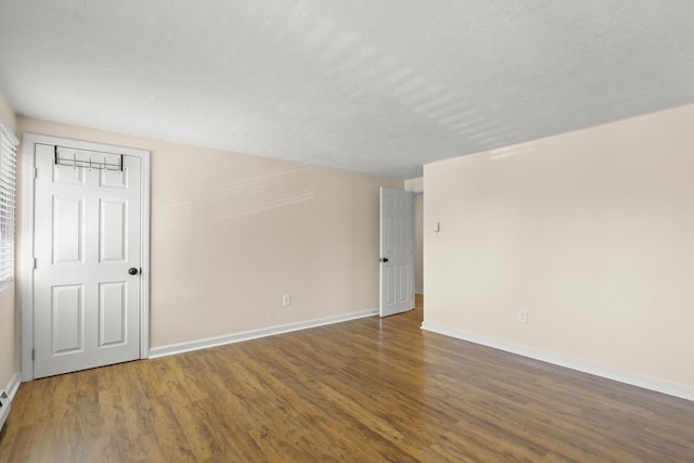 empty room with baseboards, a baseboard heating unit, and wood finished floors