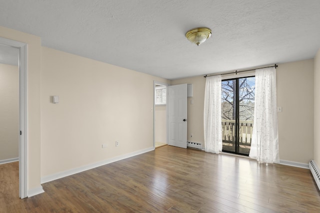 empty room featuring baseboard heating, baseboards, wood finished floors, and a textured ceiling